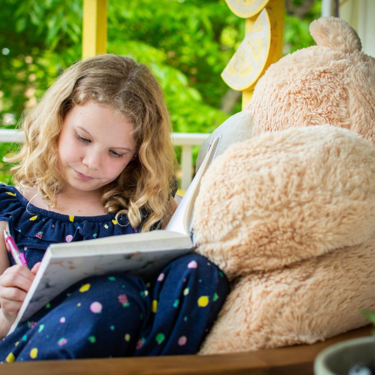 little girl writing with bear on side