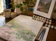 Partially completed paint by numbers canvas surrounded by paint pots and brushes on a wooden table